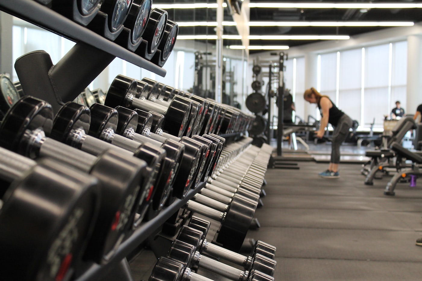 Rack of dumbbells on a gym floor with a member training in the background